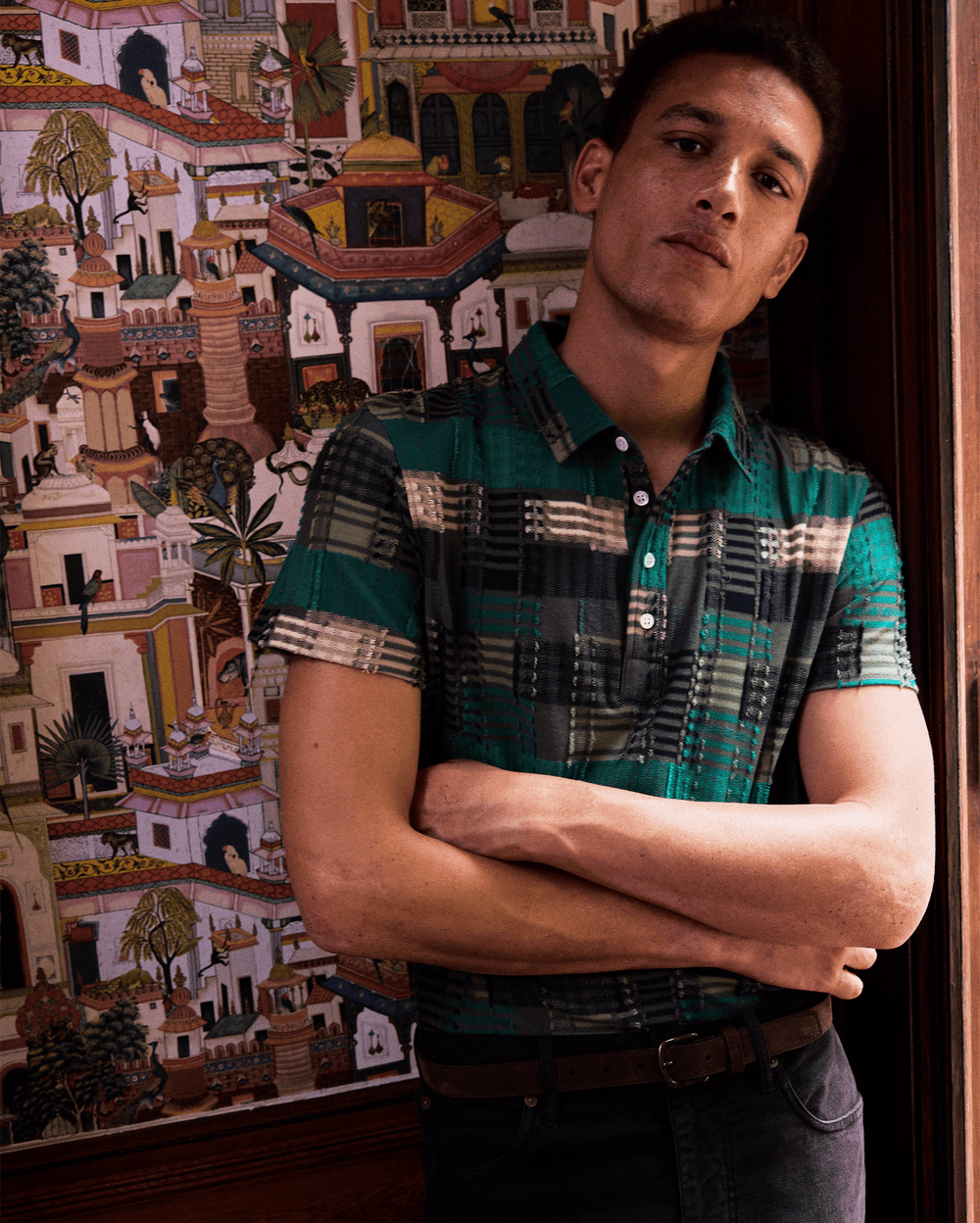 Man standing with arms crossed in front of a colorful tapestry