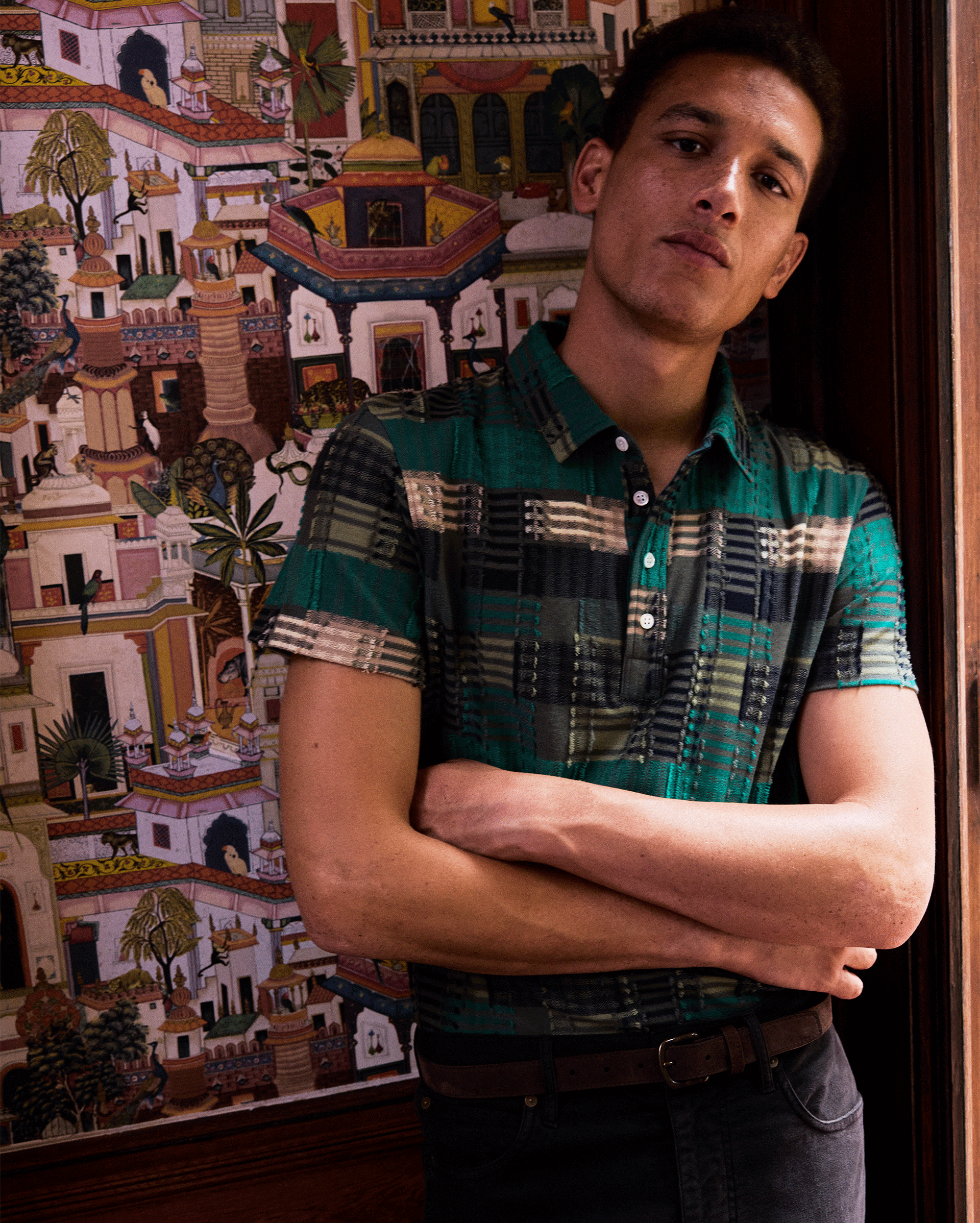Man standing with arms crossed in front of a colorful tapestry