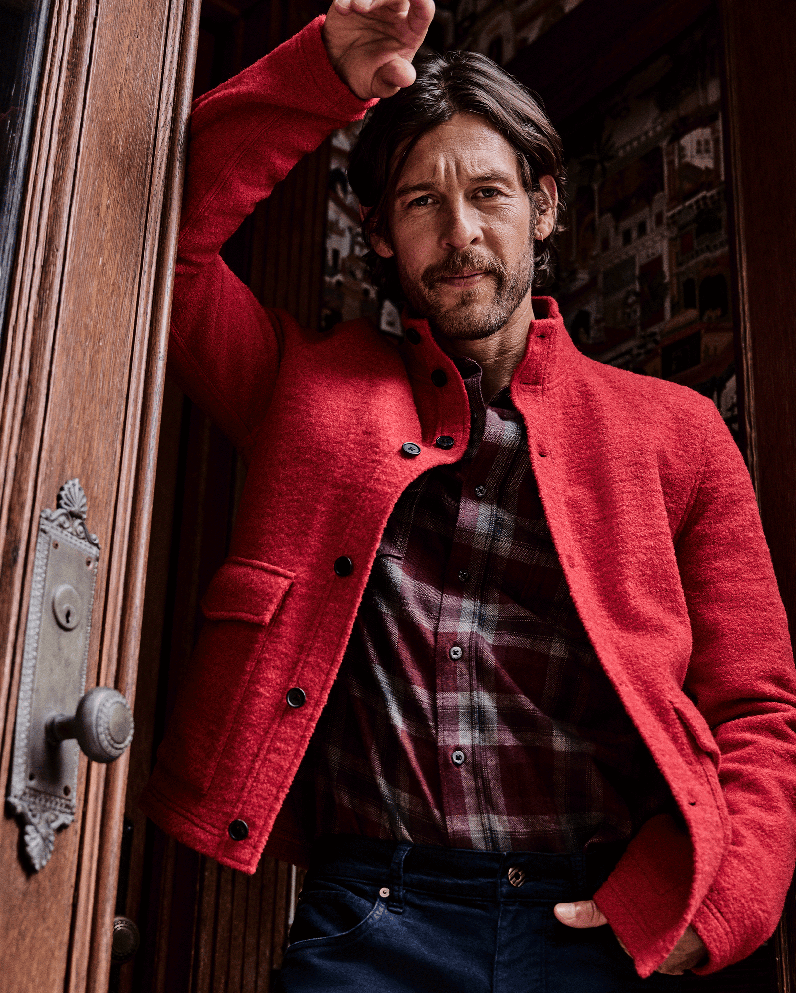 Man wearing a red coat standing in front of a wooden door.