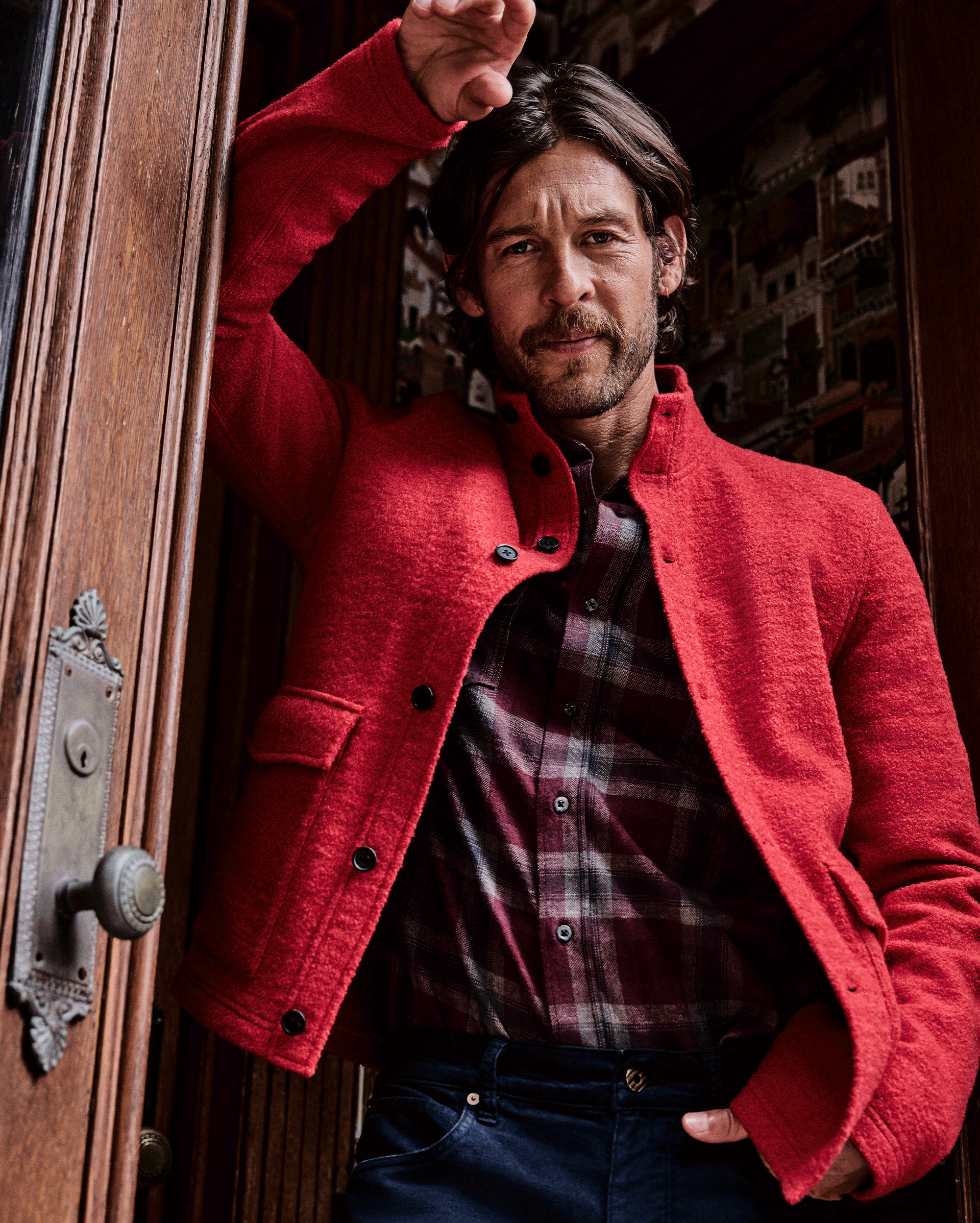 Man wearing a red coat standing in front of a wooden door.