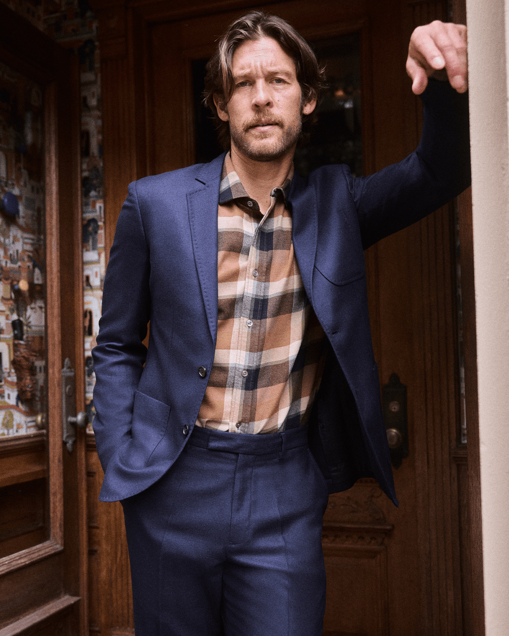 Man in a blue suit and plaid shirt standing in a doorway.