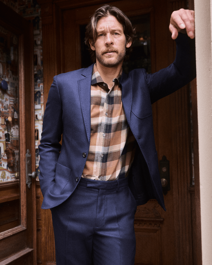 Man in a blue suit and plaid shirt standing in a doorway.