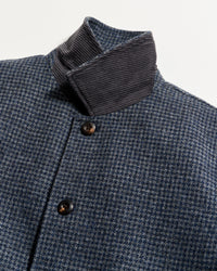 Close-up of a blue and grey houndstooth patterned coat with brown buttons and a contrasting dark gray corduroy collar, photographed against a plain white background.