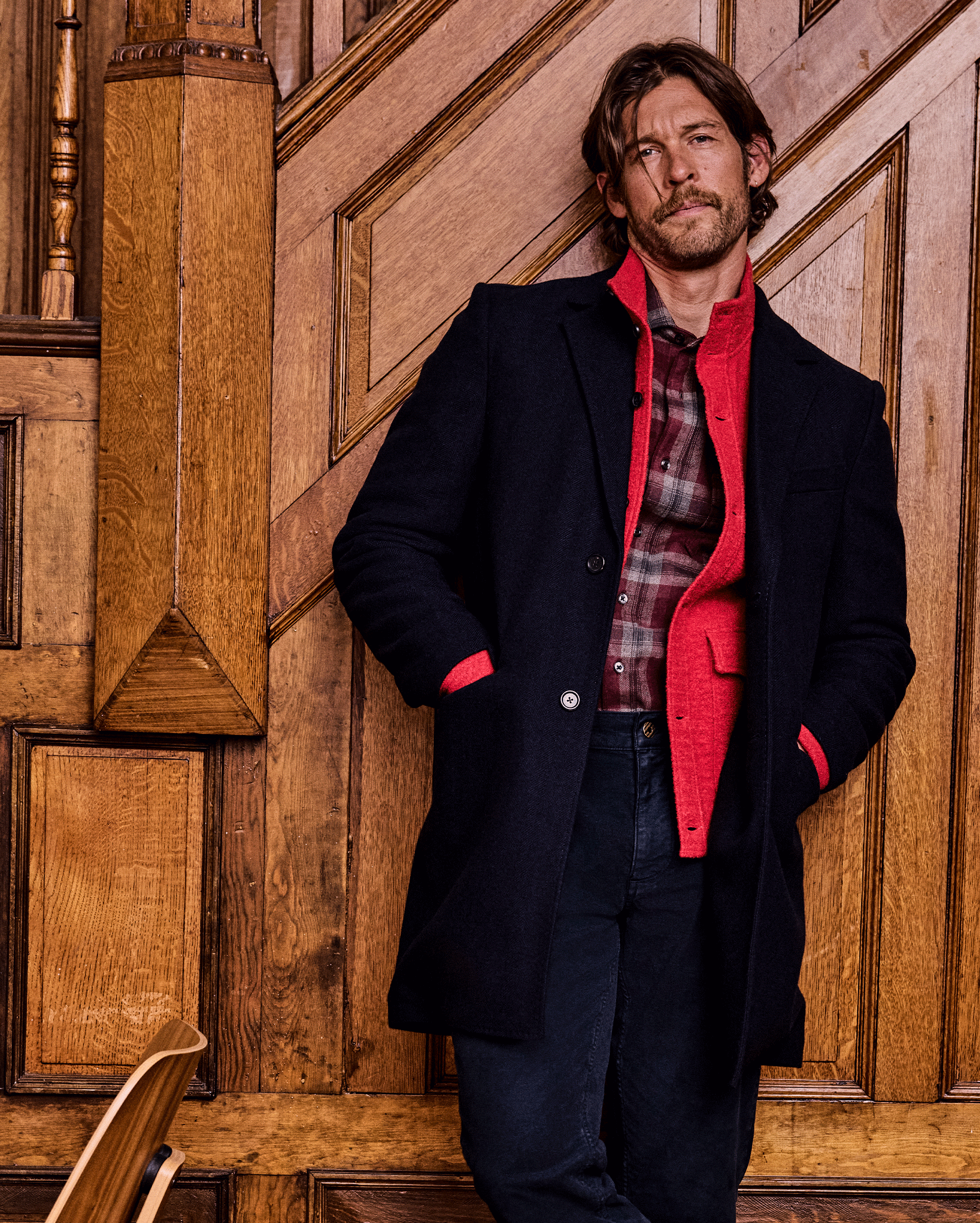 Man wearing a dark coat with a red interior against a wooden paneled wall