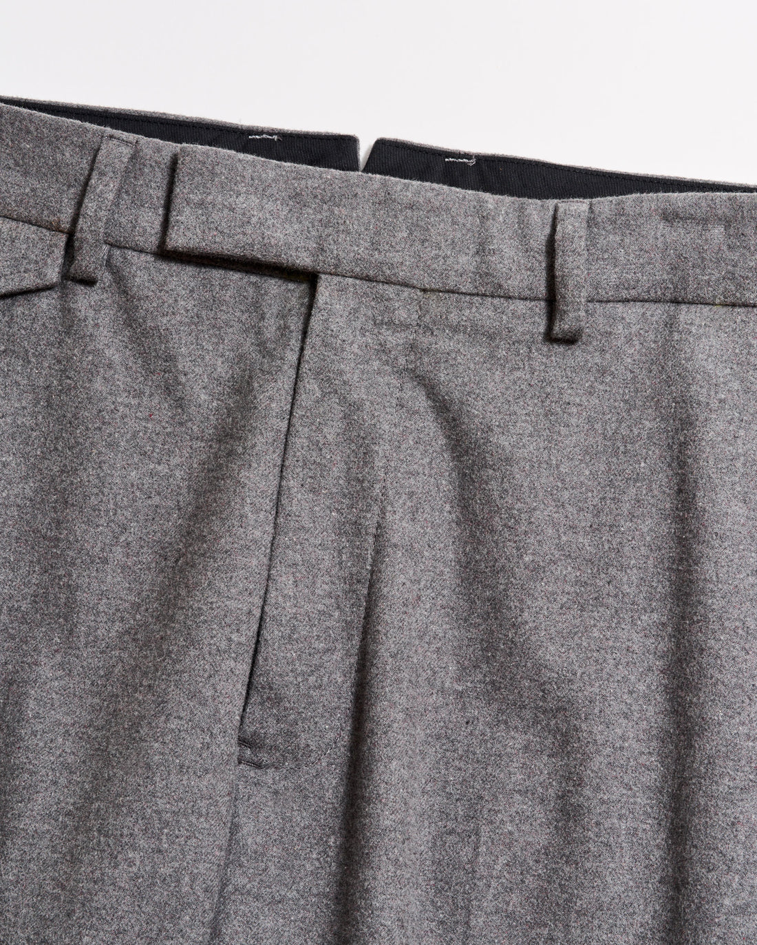 Close-up of the waistband and upper section of a pair of grey dress trousers, showing belt loops, pleats, and part of the zipper area against a plain background.