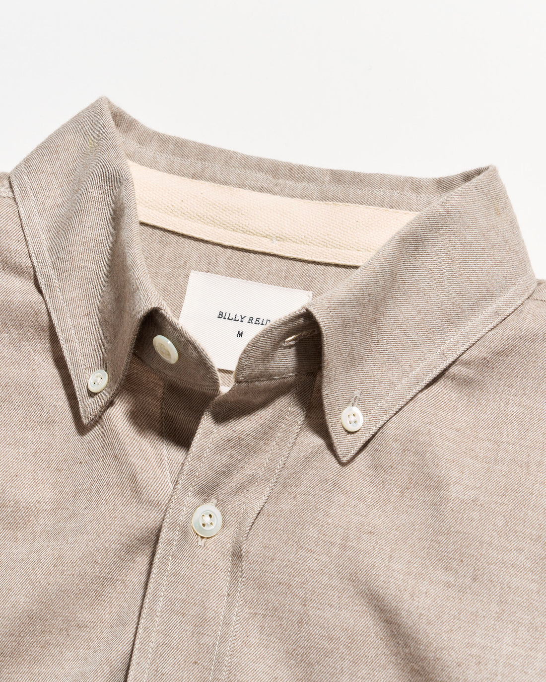 Close-up of a light beige button-down shirt collar with white buttons and a visible Billy Reid neck label.