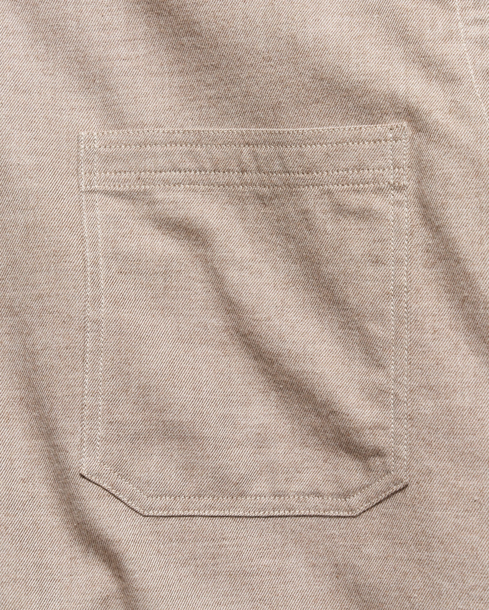 Close-up of a light beige colored fabric pocket with clean, matching stitching on a textured woven garment.