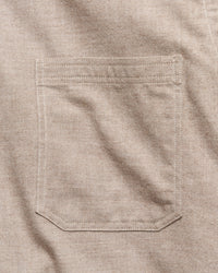 Close-up of a light beige colored fabric pocket with clean, matching stitching on a textured woven garment.