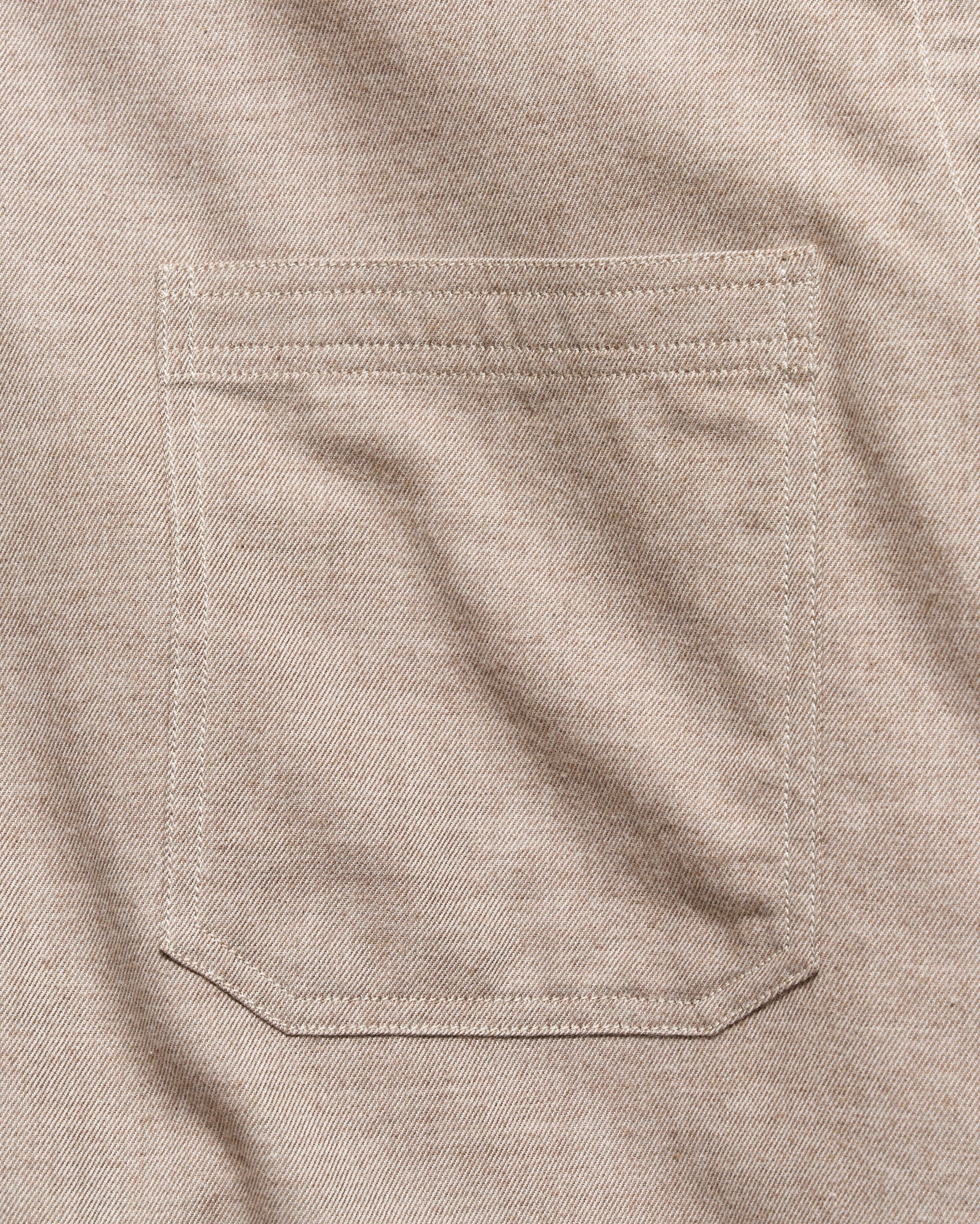 Close-up of a light beige colored fabric pocket with clean, matching stitching on a textured woven garment.