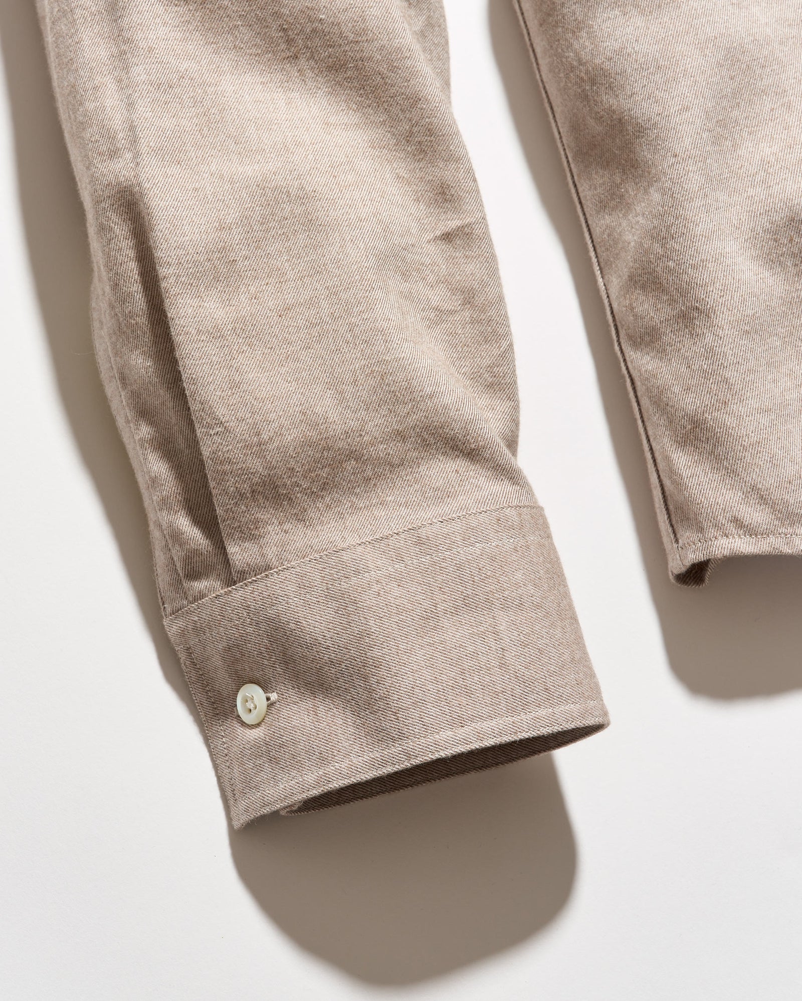 Close-up of a beige cotton shirt sleeve with a buttoned cuff, laid flat on a light background.
