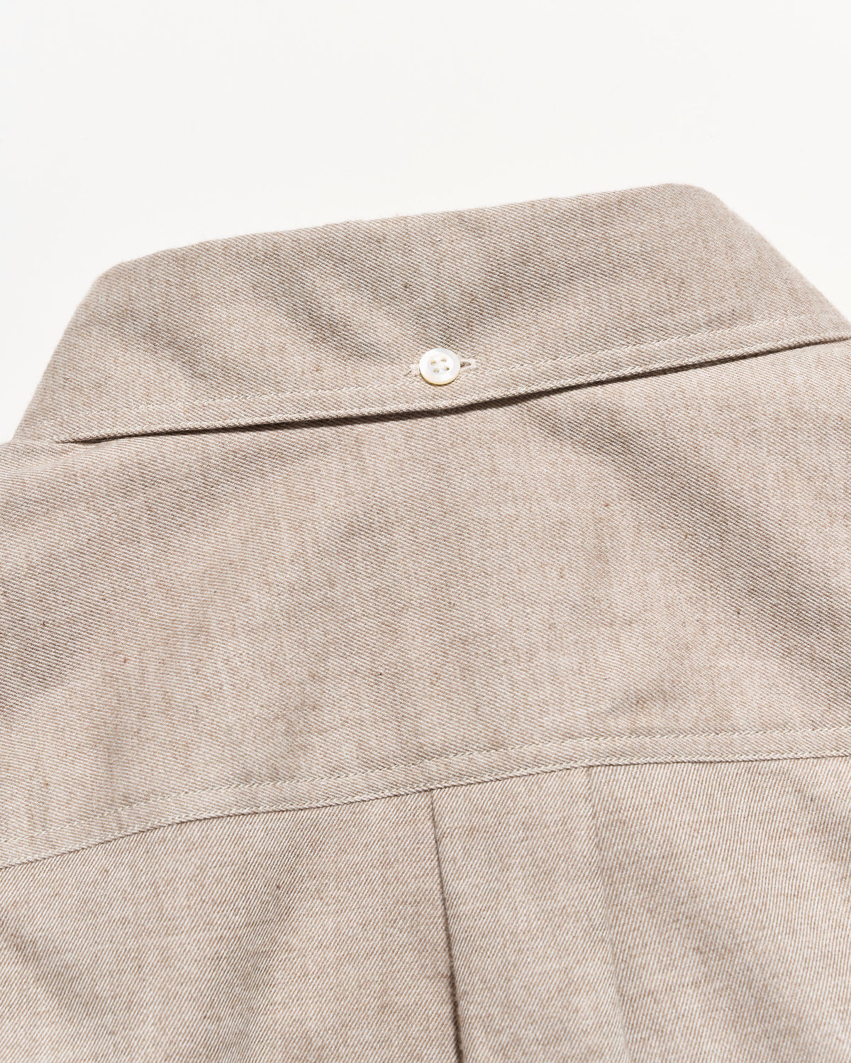 Close-up of a light beige textured fabric garment, showing the back collar with a single white button and a vertical seam below.
