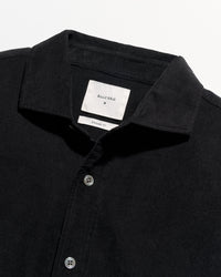 Close-up of a black button-up shirt with a pointed collar and a white neck label reading Billy Reid.