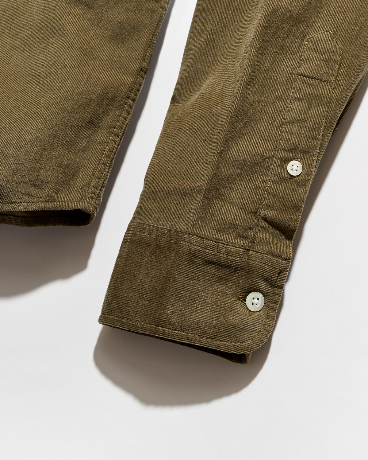 Close-up of an olive green corduroy garment sleeve with two white buttons on a light gray background.