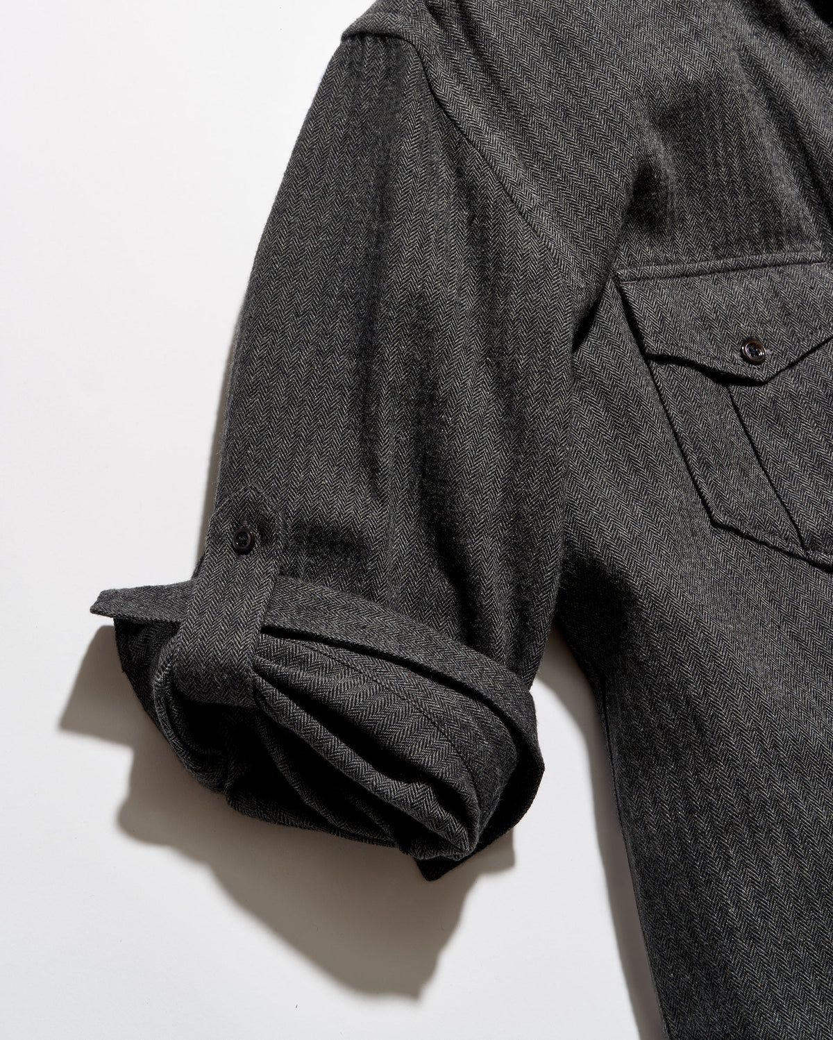 Close-up of a dark charcoal gray shirt jacket with a rolled-up sleeve and a buttoned chest pocket, laid flat on a white background.