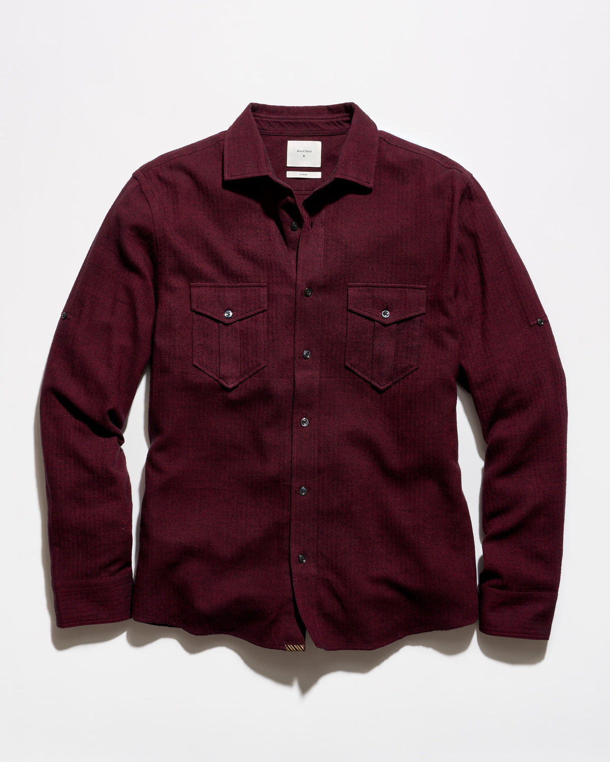 A long-sleeve button-up shirt in deep burgundy with two buttoned chest pockets, laid flat against a light gray background.