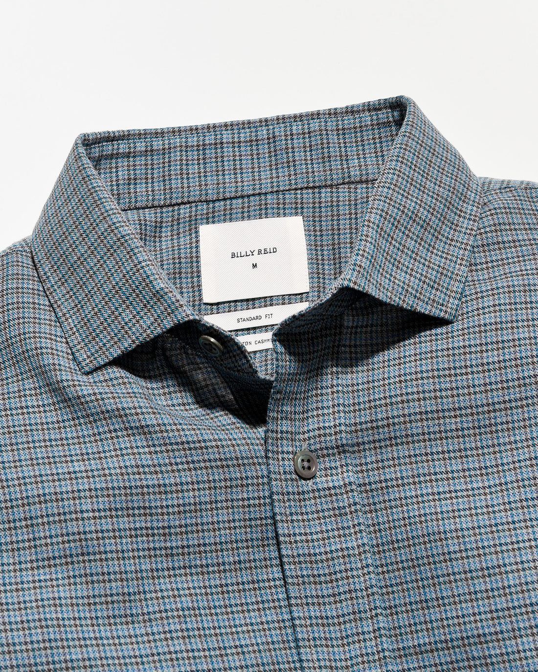 Close-up of a Billy Bag designator plaid button-down shirt in blue, gray, and white, showing the collar, brand label, and button.