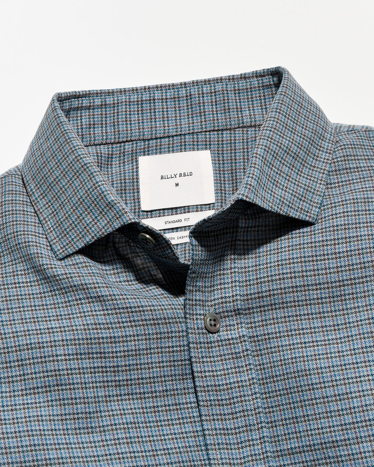 Close-up of a Billy Bag designator plaid button-down shirt in blue, gray, and white, showing the collar, brand label, and button.