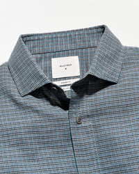 Close-up of a Billy Bag designator plaid button-down shirt in blue, gray, and white, showing the collar, brand label, and button.