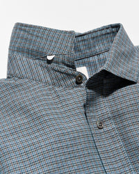 Close-up of a collared button-up shirt with a fine blue, gray, and white micro-check pattern, featuring dark brown buttons.