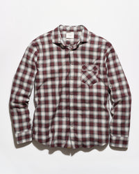 A long-sleeve button-up plaid shirt in a burgundy, white, and gray checkered pattern, featuring a single chest pocket, laid flat against a light gray background.
