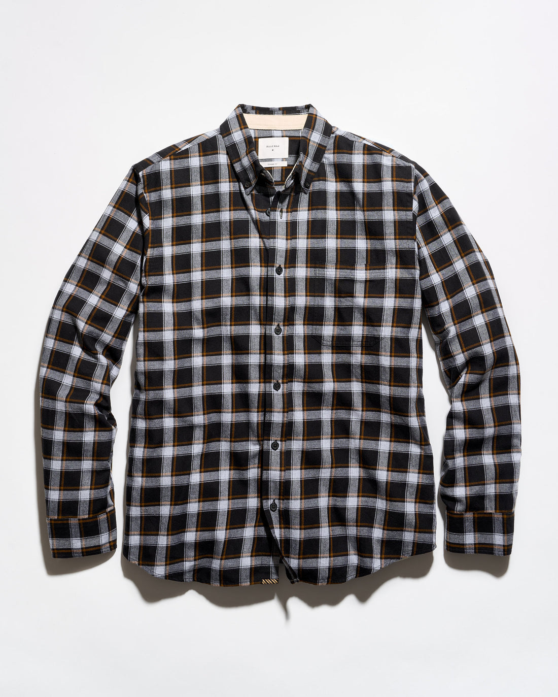 A long-sleeve button-down plaid shirt in black, white, and thin orange stripes, laid flat against a light gray background.