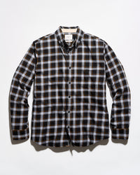 A long-sleeve button-down plaid shirt in black, white, and thin orange stripes, laid flat against a light gray background.