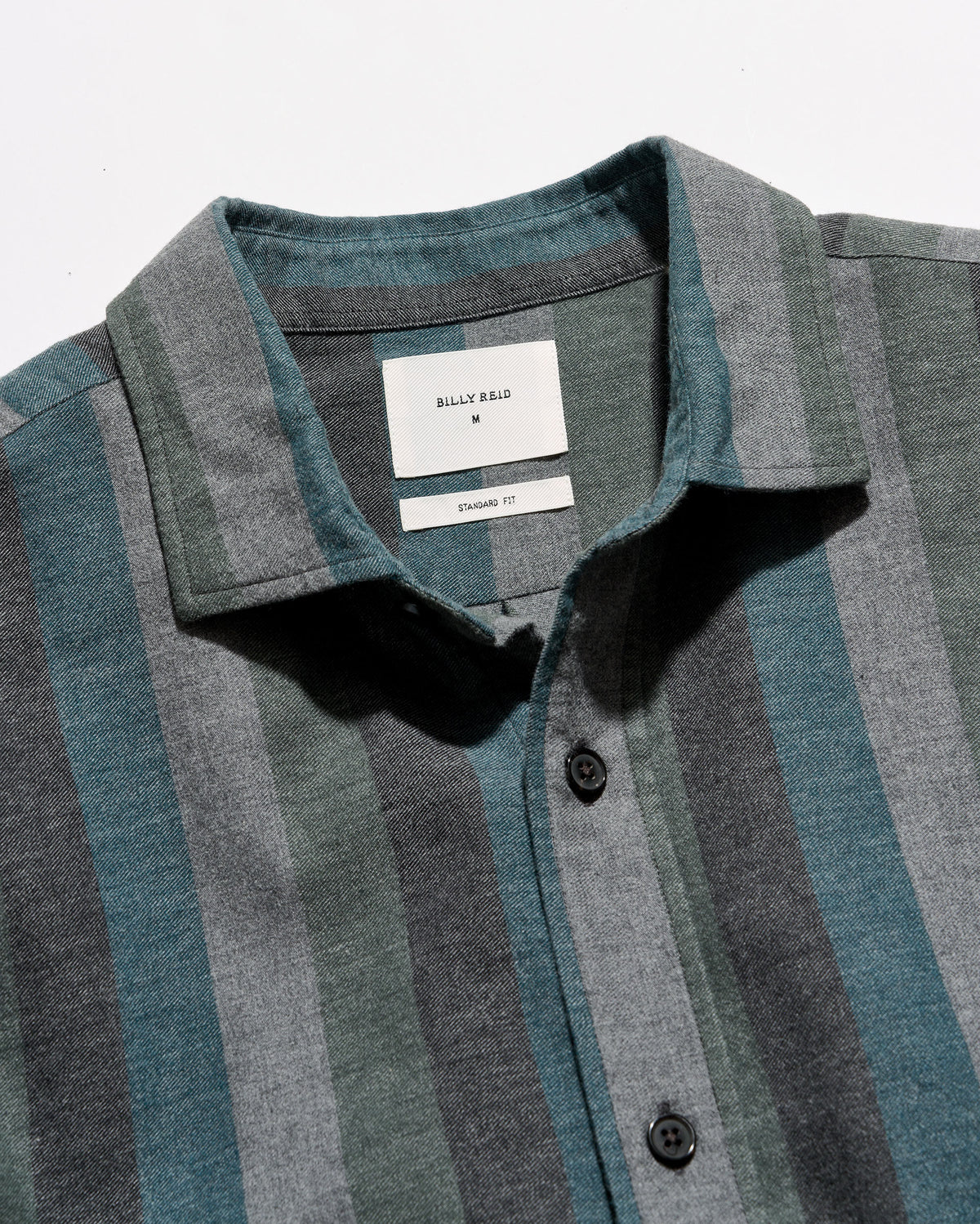 Close-up of a striped button-up shirt collar with a white neck label reading Billy Reid. The fabric has vertical stripes in muted teal, slate blue, and charcoal gray.