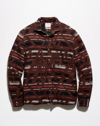 A long-sleeve button-up shirt with a geometric pattern in dark red, black, and off-white, laid flat against a light gray background.