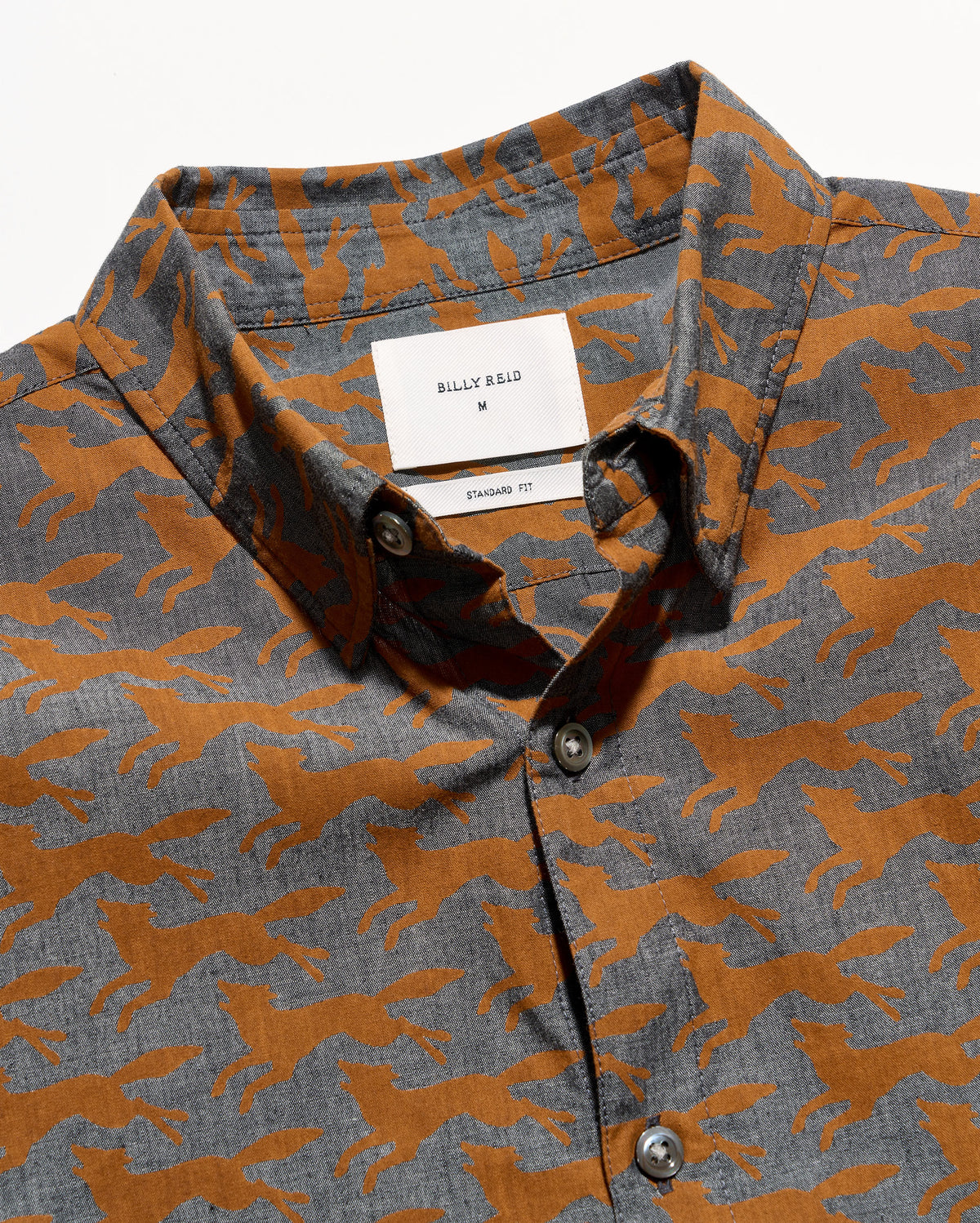 Close-up of a Billy Reid button-down shirt featuring an allover running foxpattern in rust orange and heather gray, with a white brand label visible at the collar.