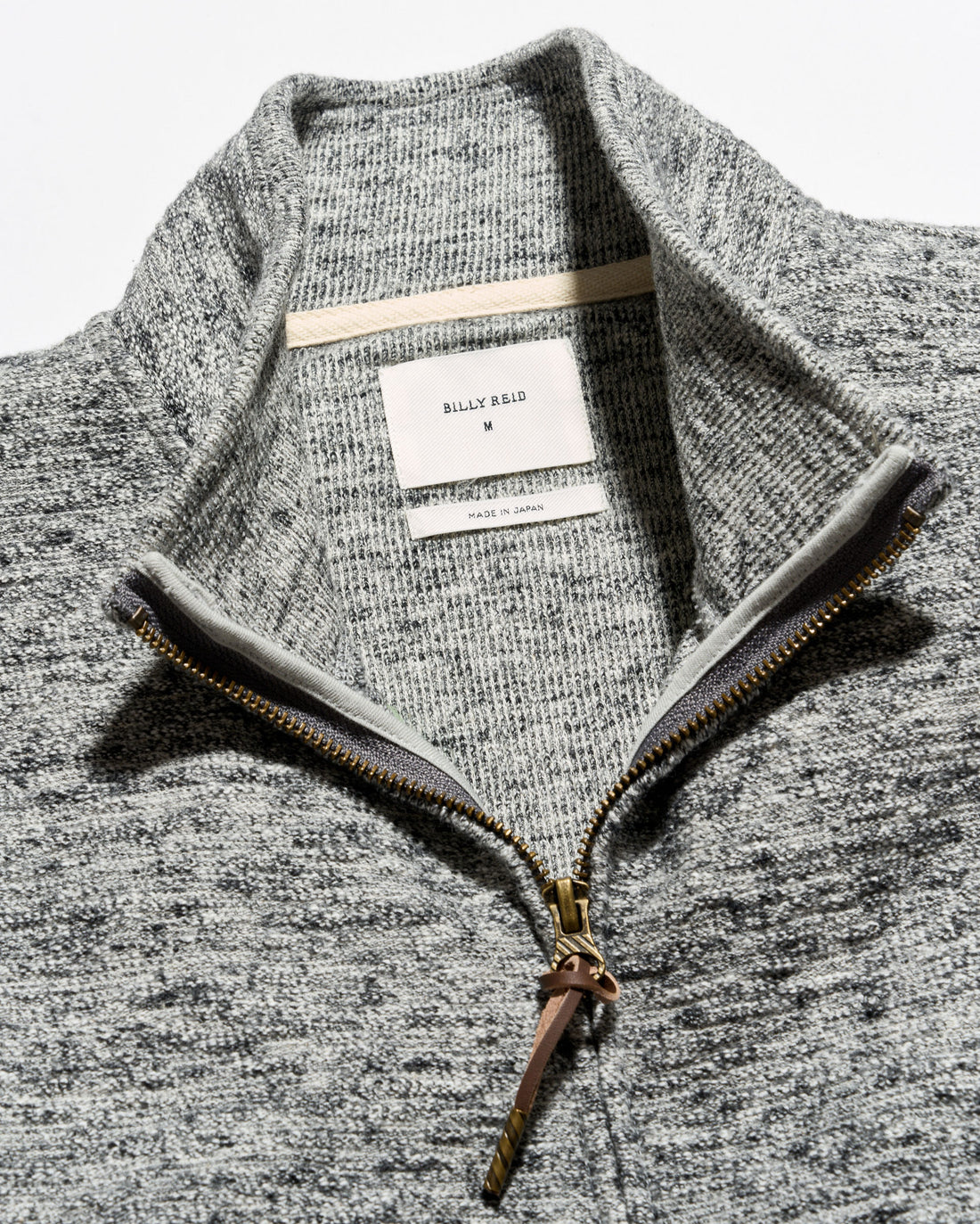 Close-up of a gray heathered knit quarter-zip sweater with a stand collar, showing a white neck label that reads Billie Eilil and a gold-toned zipper.