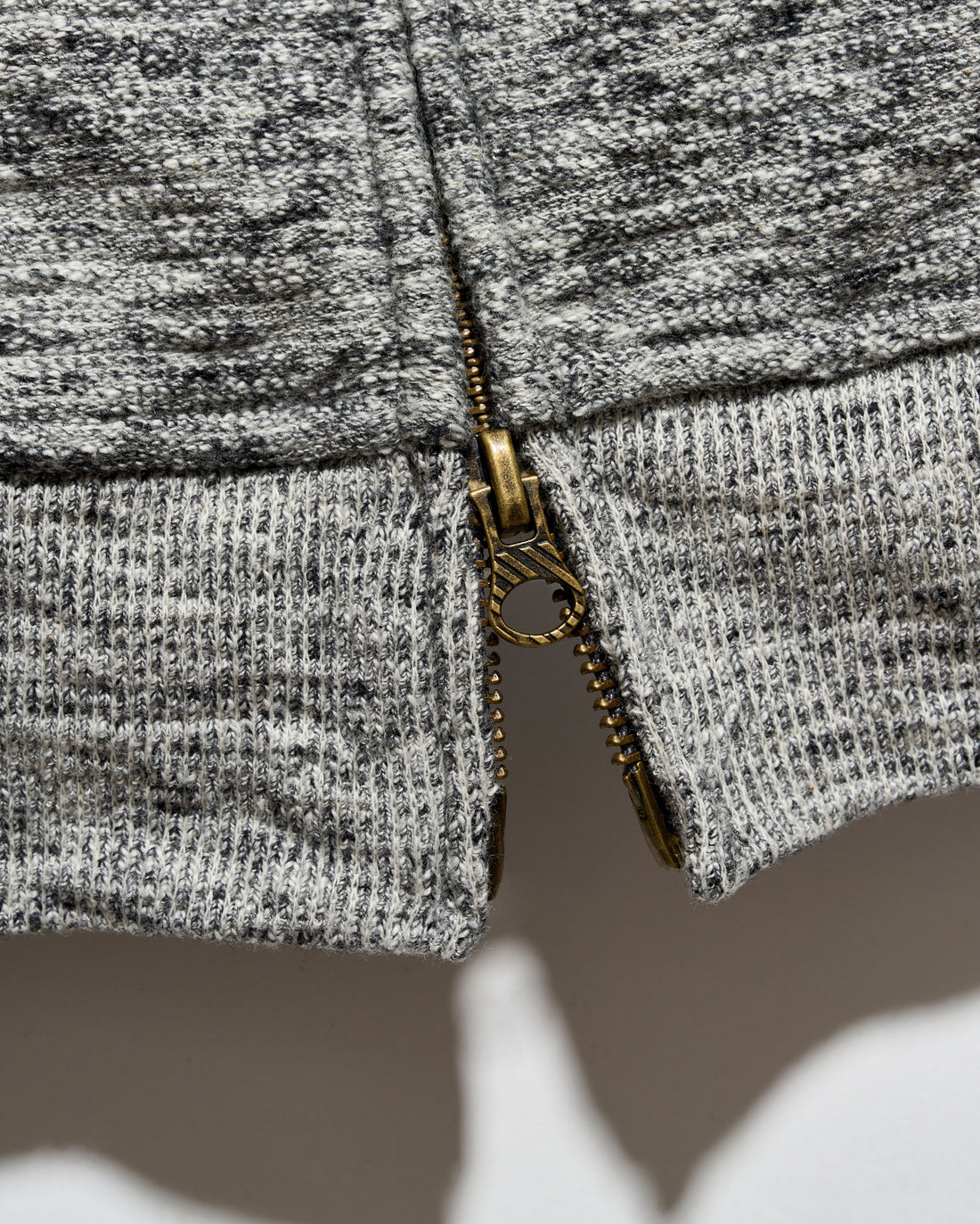 Close-up of a gray and black heathered knit fabric with a gold-tone metal zipper running vertically down the center.
