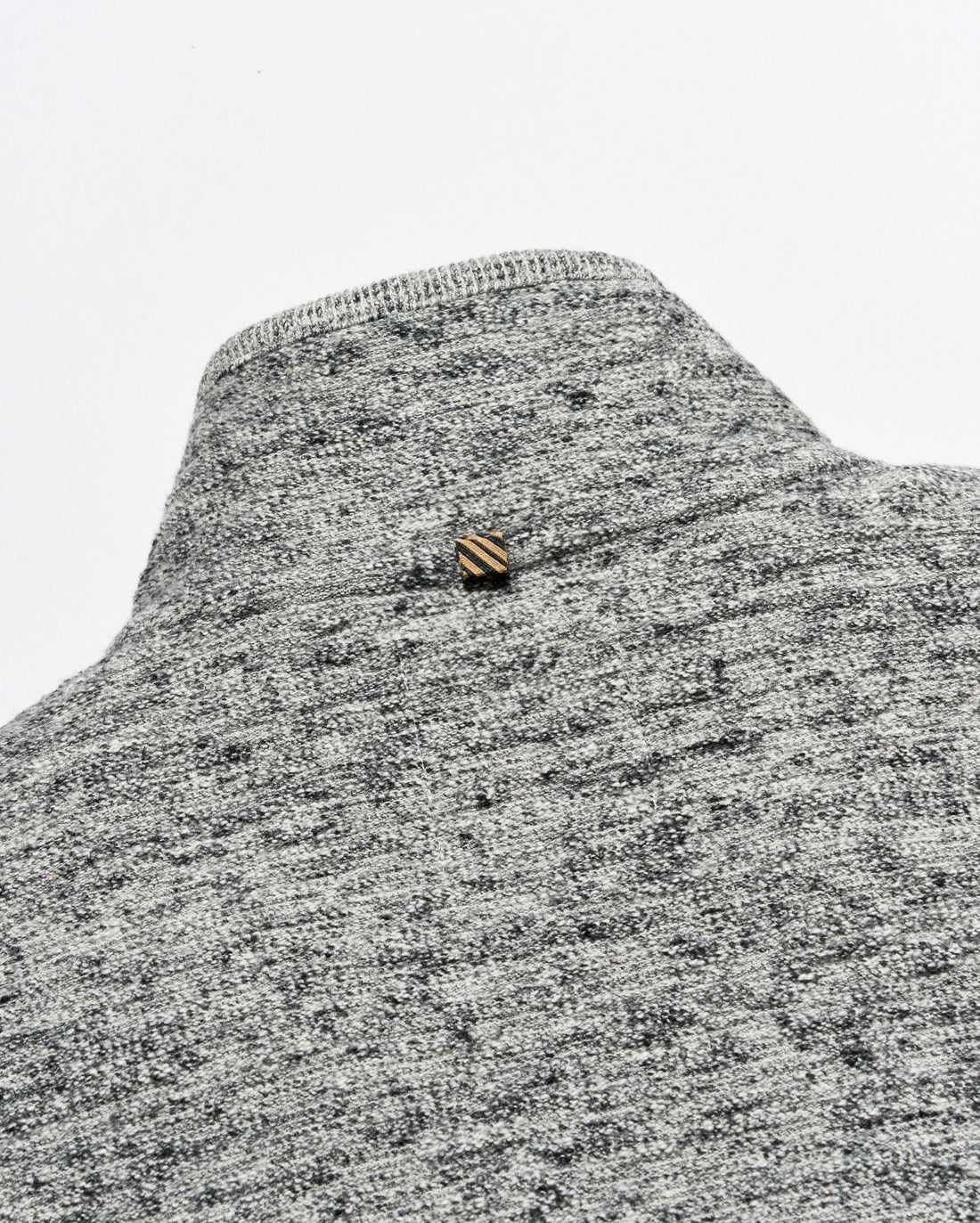 Close-up of a gray and white heather knit sweater or knit garment with a small striped gold and brown button at the neckline, set against a plain light gray background.