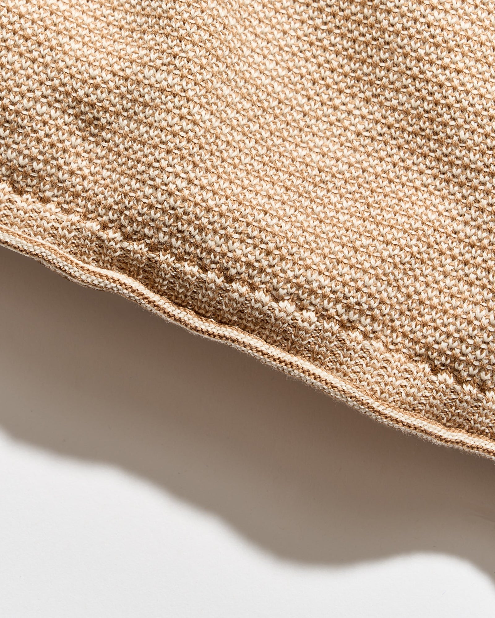 Close-up of a woven textile in a warm beige or tan color, showing the texture and edge of the material against a white background.