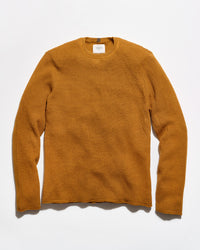 A textured waffle-knit crewneck sweater in a warm mustard yellow color, laid flat against a clean white background.