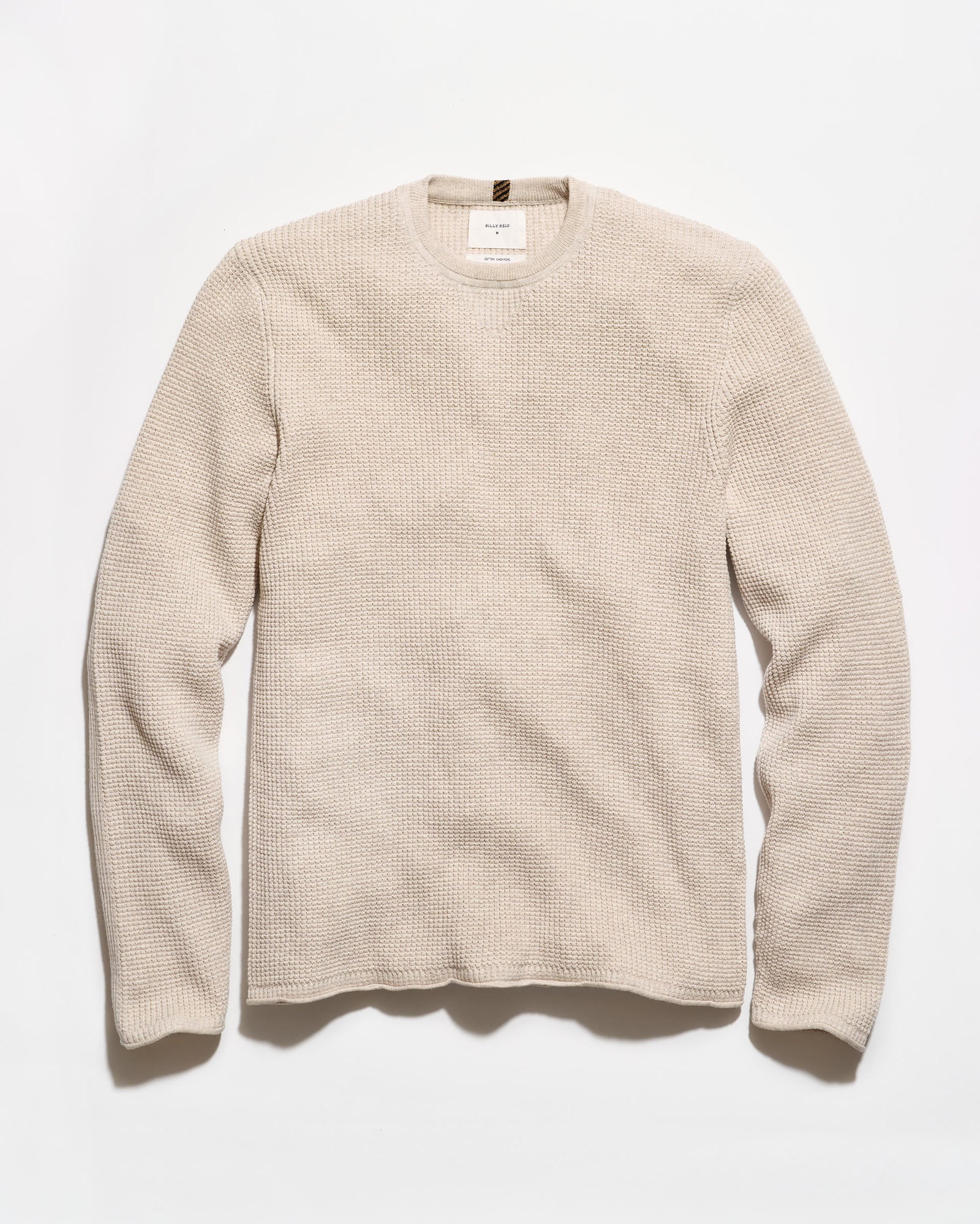 A light beige crewneck sweater with a textured waffle knit pattern, laid flat against a clean white background.