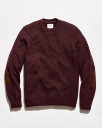 A crewneck sweater in a deep burgundy color with brown patchwork elbow patches, laid flat against a white background.