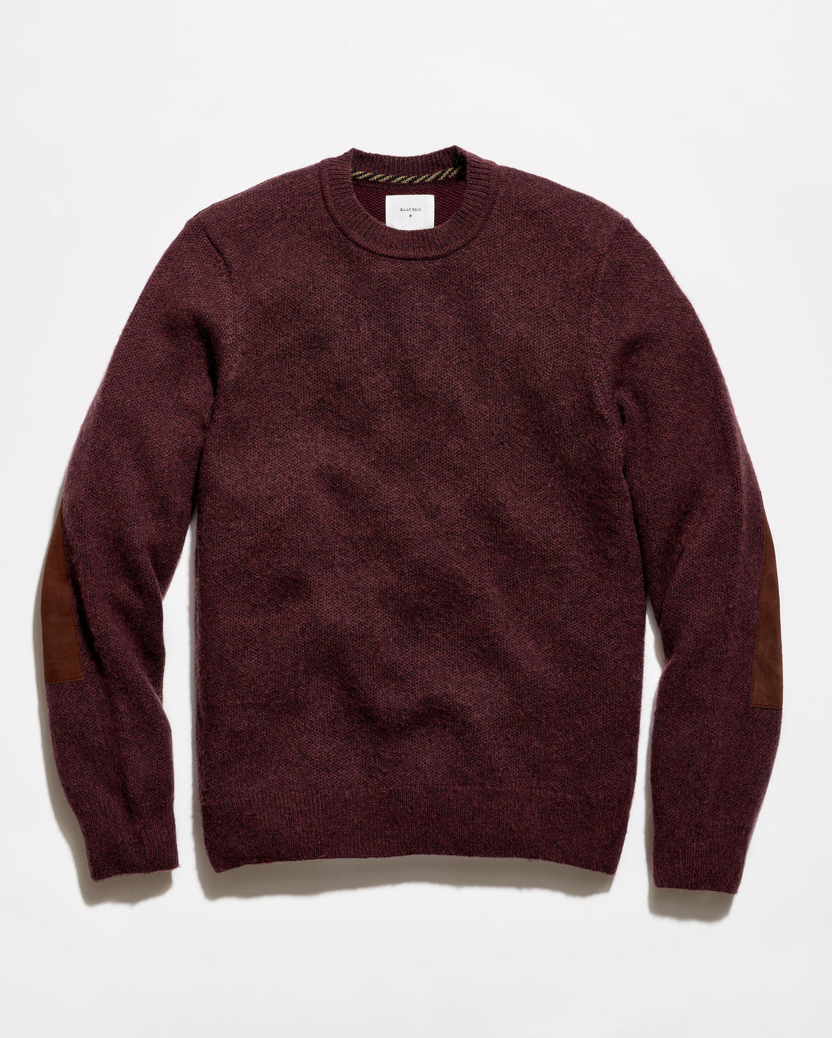 A crewneck sweater in a deep burgundy color with brown patchwork elbow patches, laid flat against a white background.