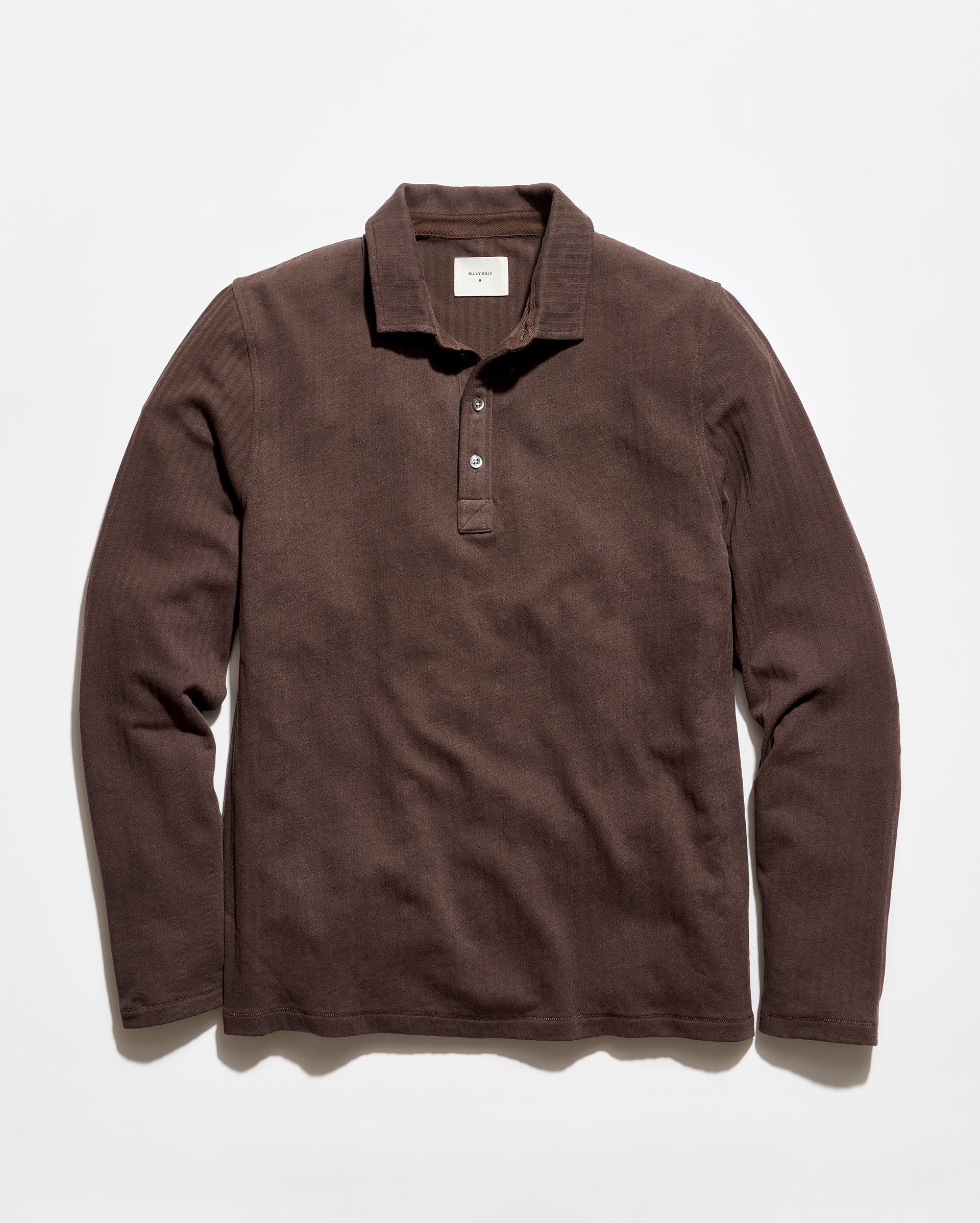 A dark brown ribbed long-sleeve polo shirt with a three-button placket, laid flat against a light off-white background.