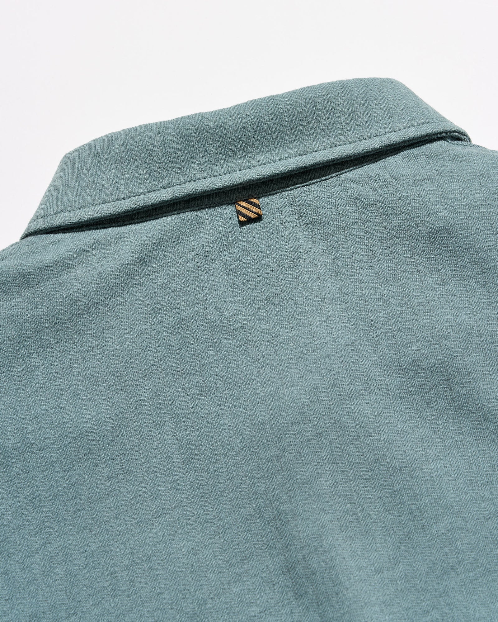 Close-up of the back collar of a heathered teal-green polo shirt, featuring a small embroidered striped logo tab.