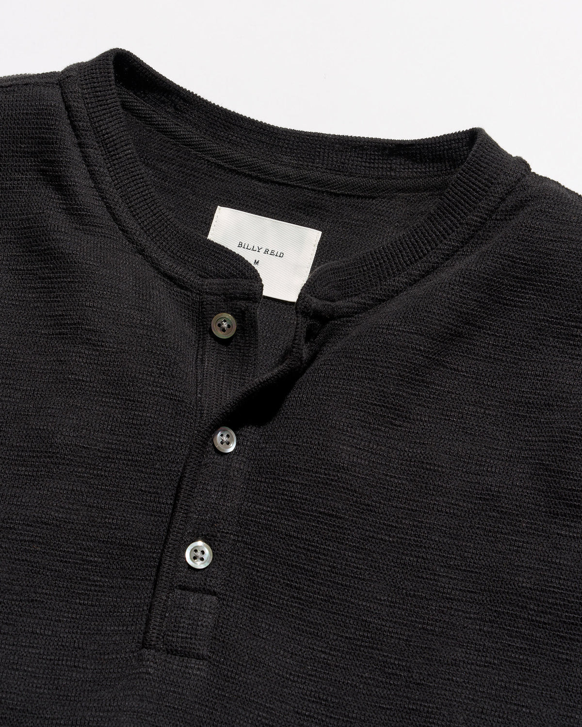 Close-up of a black ribbed Henley shirt with a three-button placket and a white neck label