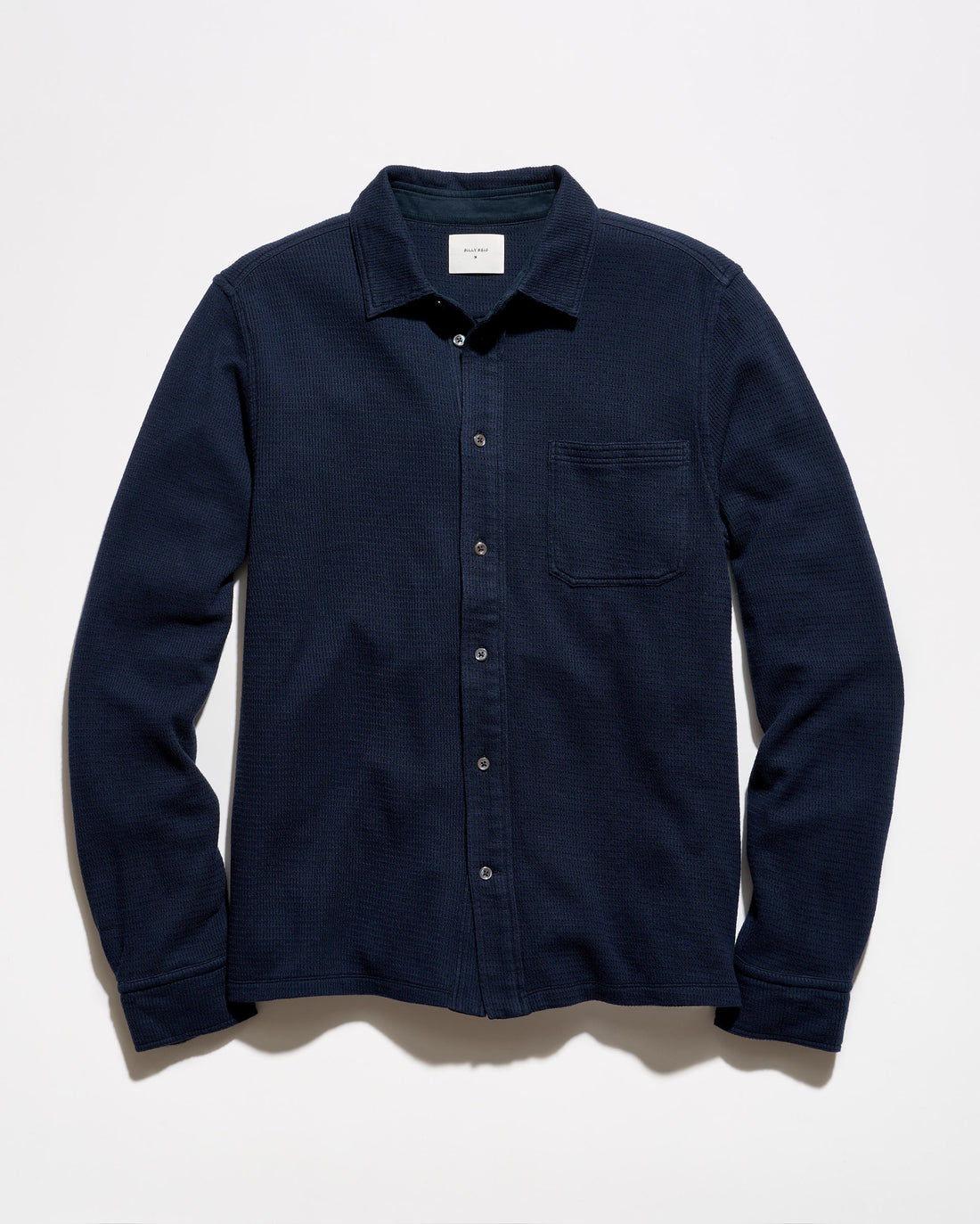 A dark navy blue long-sleeve button-up shirt with a single chest pocket, laid flat against a light off-white background.