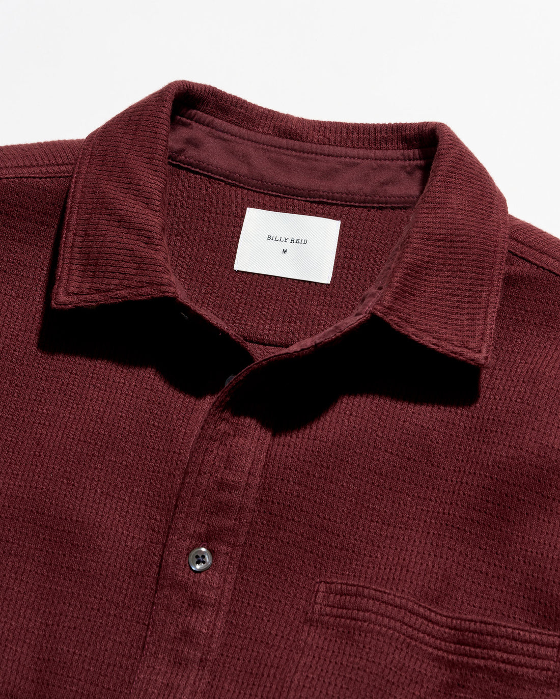 Close-up of a waffle-knit polo shirt collar in burgundy with a white inner neck label reading Billy Reid.