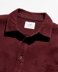 Close-up of a waffle-knit polo shirt collar in burgundy with a white inner neck label reading Billy Reid.