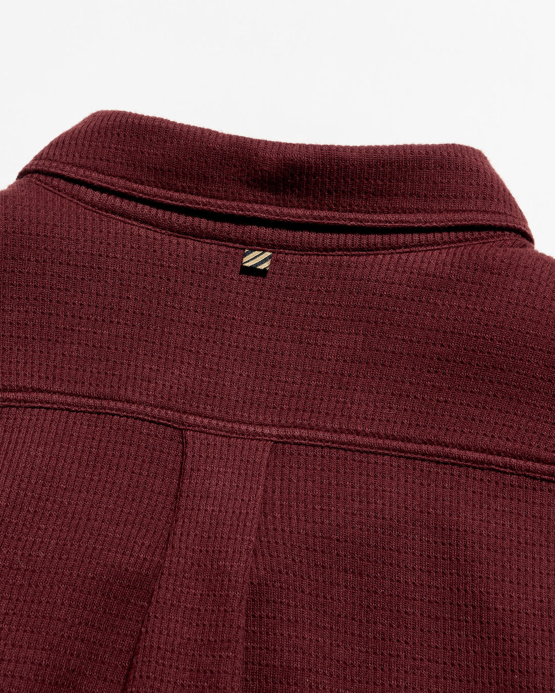 Close-up of a ladder knit button down deep burgundy, showing the collar, a small embroidered logo patch, and the textured fabric.