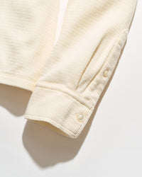 Close-up of a cream-colored ribbed knit garment sleeve with buttoned cuffs, shown on a white background with a soft shadow.