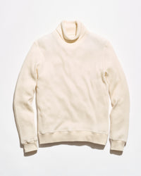A cream-colored ribbed knit turtleneck sweater laid flat against a light off-white background.