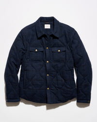 A dark navy blue quilted overshirt jacket with a subtle plaid pattern, featuring gold-tone snap buttons and two chest pockets, laid flat against a white background.
