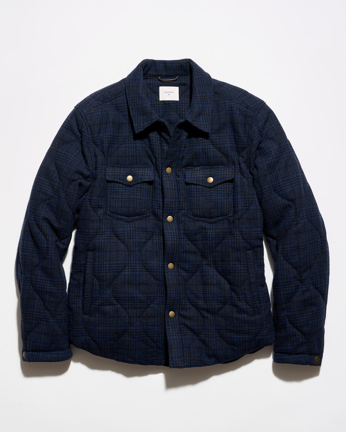 A dark navy blue quilted overshirt jacket with a subtle plaid pattern, featuring gold-tone snap buttons and two chest pockets, laid flat against a white background.