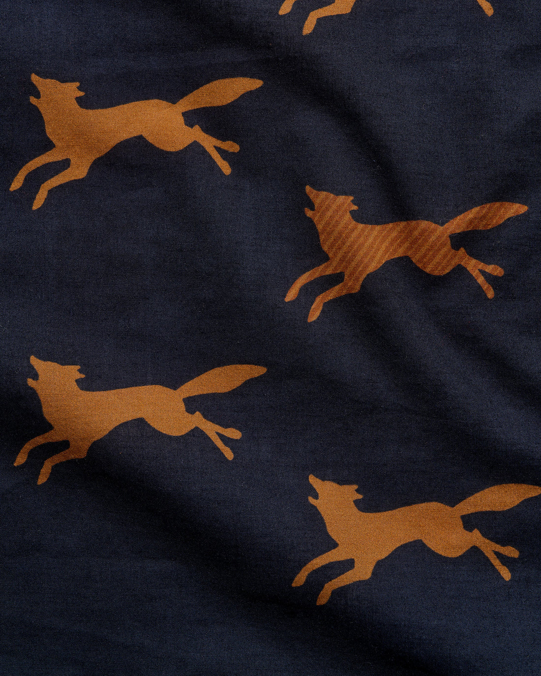 Close-up of a navy blue fabric with a repeating pattern of running foxes in a warm tan or camel color.