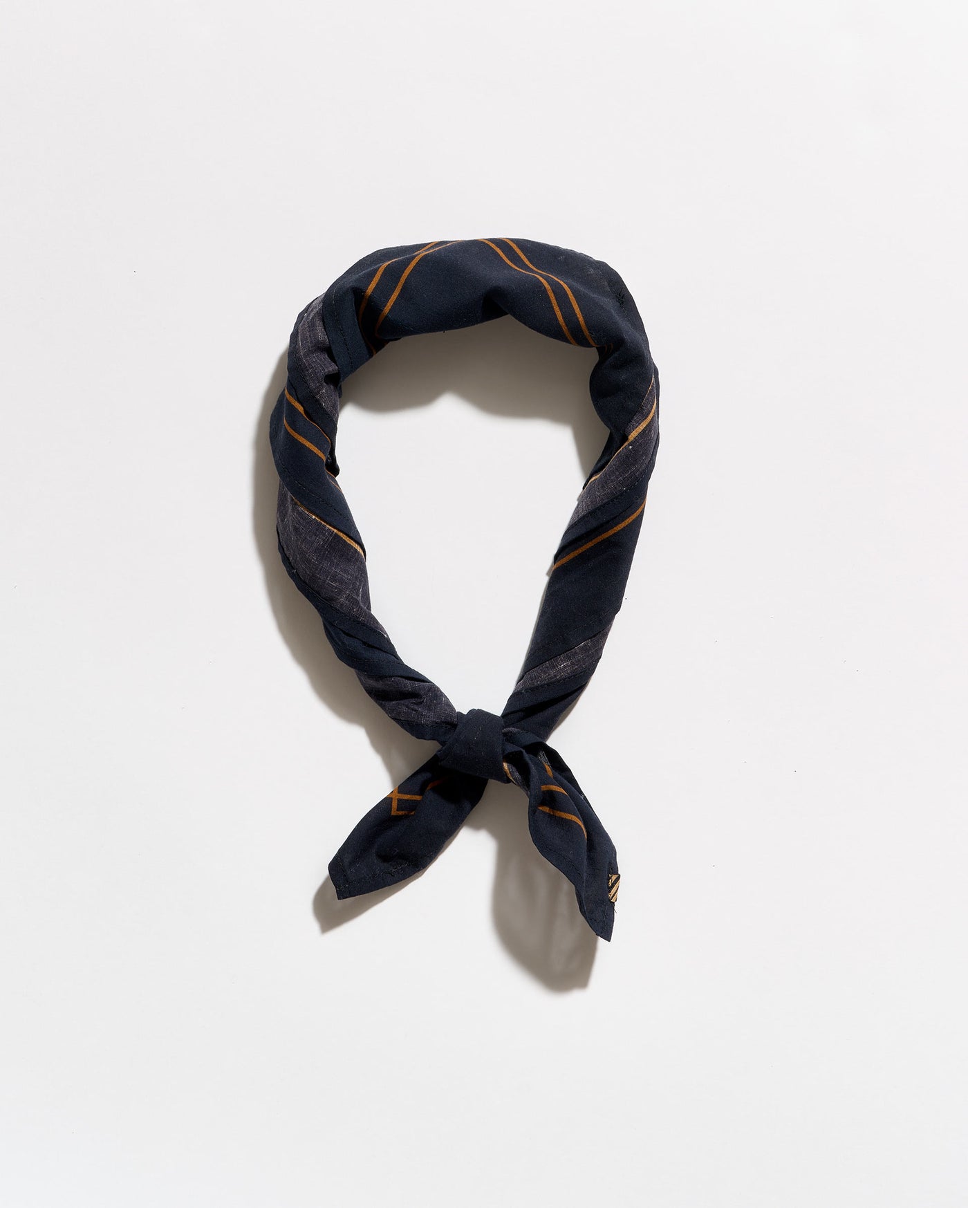 A navy blue silk scarf with thin gold stripes, knotted and looped to display its pattern, set against a plain white background.